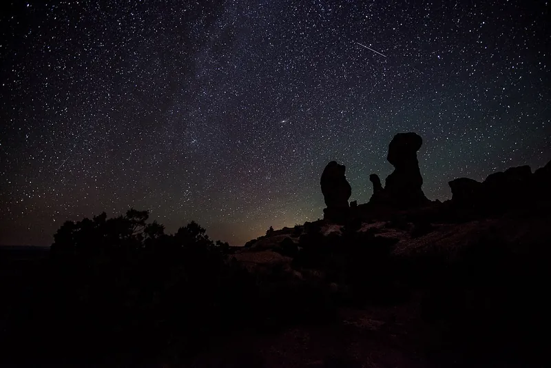 The Milky Way arcs across a dark sky above silhouetted rock pinnacles, with point-like stars.